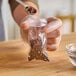 A hand using a spoon to fill a small clear plastic bag of cloves from a bowl.