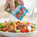 A person pouring a Hidden Valley fat free French dressing packet onto a salad.