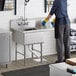 A woman standing in a professional kitchen using a Regency stainless steel one compartment sink with a drainboard.