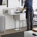 A woman washing dishes in a Regency stainless steel commercial sink with a left drainboard.
