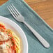 A 1880 Hospitality stainless steel dinner fork next to a plate of spaghetti with sauce.