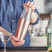 A woman using an Acopa copper cocktail shaker to pour a drink into a glass.