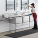 A woman in a red apron and gloves cleaning a Regency stainless steel 3 compartment sink.