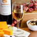 A Libbey Citation wine glass filled with white wine next to a bowl of nuts and grapes.