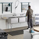 A man washing a Regency stainless steel three compartment sink.