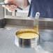 A person using a stainless steel egg ring to cook eggs in a pan.