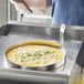 A person using a Choice stainless steel egg ring to cook eggs in a pan.