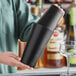 A person holding a black Acopa Boston shaker set on a counter in a cocktail bar.