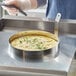 A person using a Choice stainless steel egg ring to cook eggs in a pan.