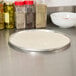 A pizza on a metal pan with spices on the counter.