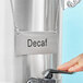 A person using a Choice silver metal coffee chafer urn with a "Decaf" label.