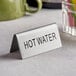 A silver stainless steel double sided "Hot Water" table tent sign on a counter.