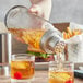 A person using an Acopa mason jar cocktail shaker to pour liquid into a glass.