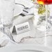 A white table with a stainless steel "Reserved" table tent next to a glass of liquid.