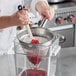 A person using a Choice stainless steel strainer to pour liquid into a container.