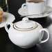 A white porcelain sugar bowl with gold trim on a table.