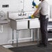 A man in a professional kitchen using a Regency stainless steel two compartment sink.