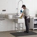 A man washing a Regency stainless steel commercial sink with 2 drainboards.