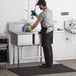 A man wearing yellow gloves cleaning a Regency stainless steel two compartment sink.