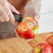 A hand using a Choice 6" Floating Vegetable Peeler to peel a red apple.