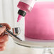 A person using a Chefmaster blushing pink airbrush color to spray a cake pink.