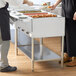 A group of people standing next to a commercial steam table with Avantco STE-3S steam table pans.