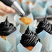 A hand using a Chefmaster Black Diamond Liqua-Gel to frost a cupcake black.