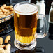 A customizable plastic beer mug filled with beer on a table with peanuts.