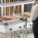 A man in a white shirt using a ServIt tubular fixed tray slide to serve food from a steam table at a buffet.