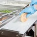 A person in blue gloves using an Avantco cutting board to cut bread.