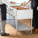 A man and woman standing next to a buffet with an Avantco electric steam table on it.