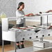 A woman serving food at a hotel buffet using an Avantco open well steam table with sneeze guard.
