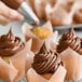 A hand using a pastry bag to pipe brown frosting on a cupcake.
