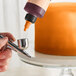 A finger holding a bottle of Chefmaster Neon Brite Orange airbrush color.