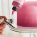 A hand using Chefmaster Deep Pink Airbrush Color to spray a pink cake.