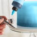 A person using a silver airbrush to paint a cake blue with Chefmaster Neon Brite Blue food coloring.