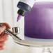 A person using a silver airbrush to spray purple color over a cake.