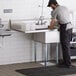 A man in an apron washing dishes in a Regency commercial sink with a left drainboard.