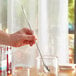 A close-up of a hand holding an Acopa silver Japanese bar spoon in a glass.