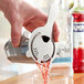 A hand using an Acopa silver Hawthorne strainer to pour a drink from a shaker into a glass.