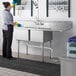 A woman in a professional kitchen cleaning a Regency stainless steel 2 compartment sink.