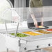 A woman using a ServIt self-service sneeze guard on a steam table.