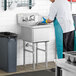 A man in a white shirt and blue apron and gloves washing a Regency stainless steel commercial sink.