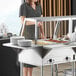 A woman standing behind a ServIt angled sneeze guard on a buffet table.