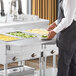 A man in a chef's uniform uses a ServIt solid drop down side tray slide on a steam table to prepare food.