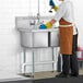 A man in an apron washing dishes in a Regency two compartment commercial sink.