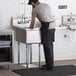 A man standing in a Regency stainless steel commercial sink with a drainboard.