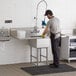 A man washing a Regency stainless steel commercial sink in a professional kitchen.