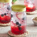 Two Acopa Rustic Charm mason jars filled with red and blue fruity drinks and blueberries on a table in a cocktail bar.