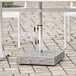 A white table with a Lancaster Table & Seating gray granite umbrella base on a stone patio.